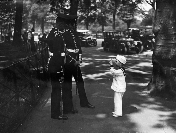 A young boy dressed in a sailor suit talking to two Grenadier Guards in a park by E. Bacon, 8th June 1925